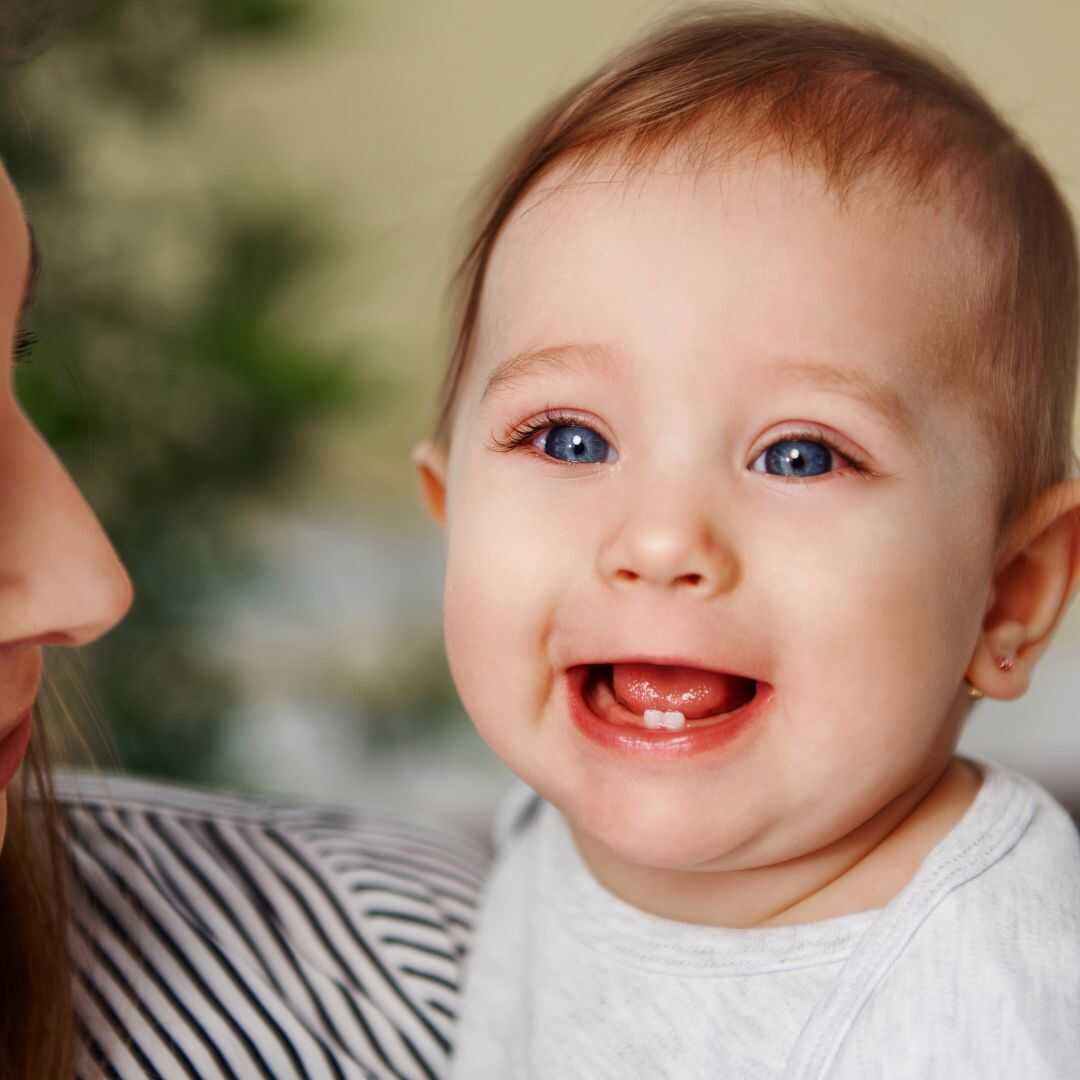 A laughing baby showing two erupted lower front teeth