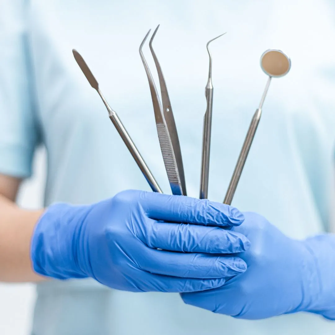 A gloved hand holding dental instruments including a mirror, probe, scaler and tweezers