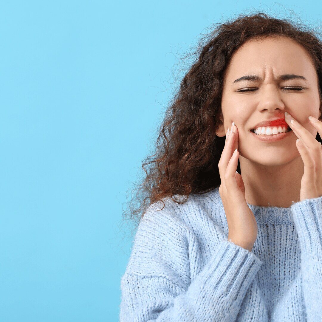 A woman holding her cheek in discomfort from gum pain