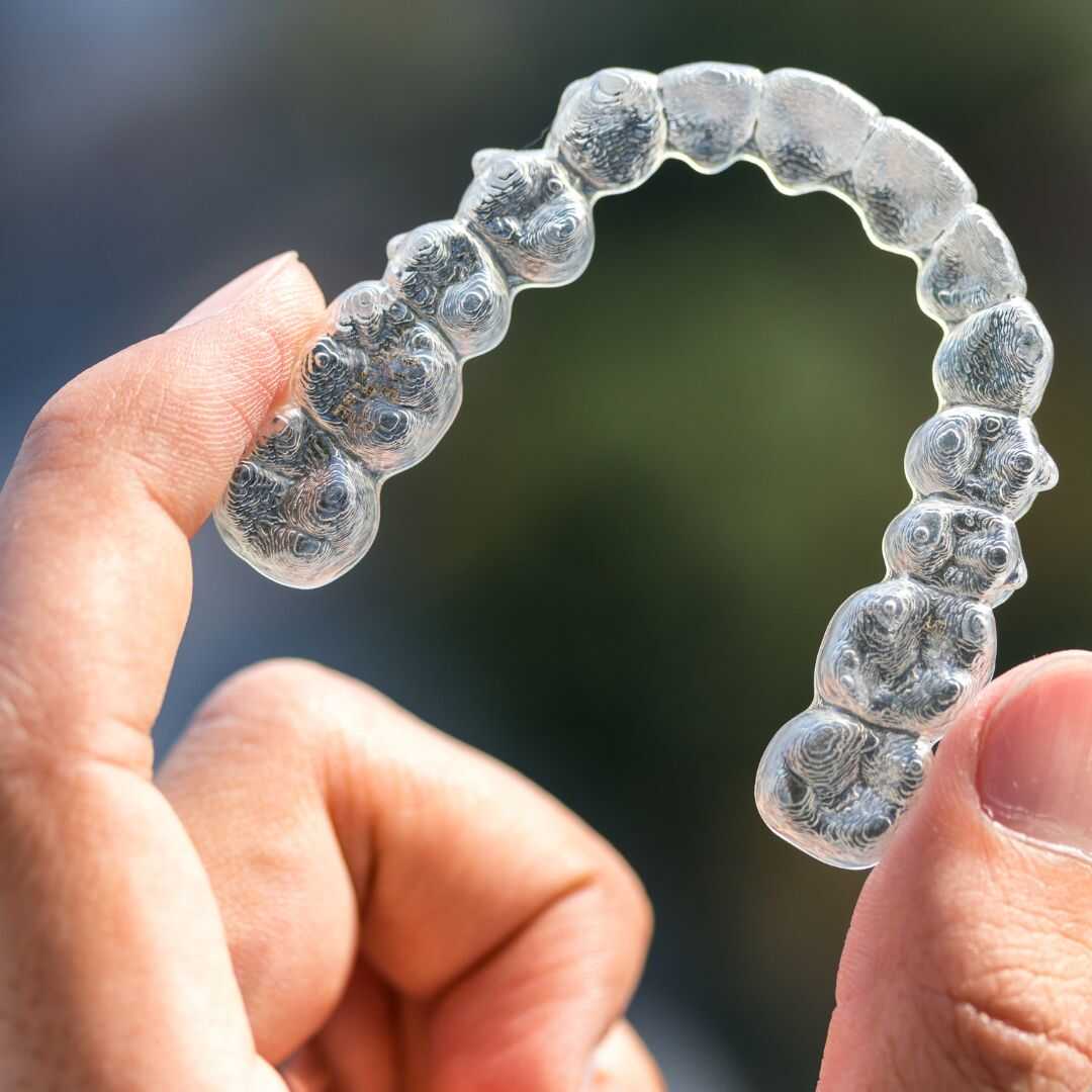 A clear aligner tray held between finger and thumb