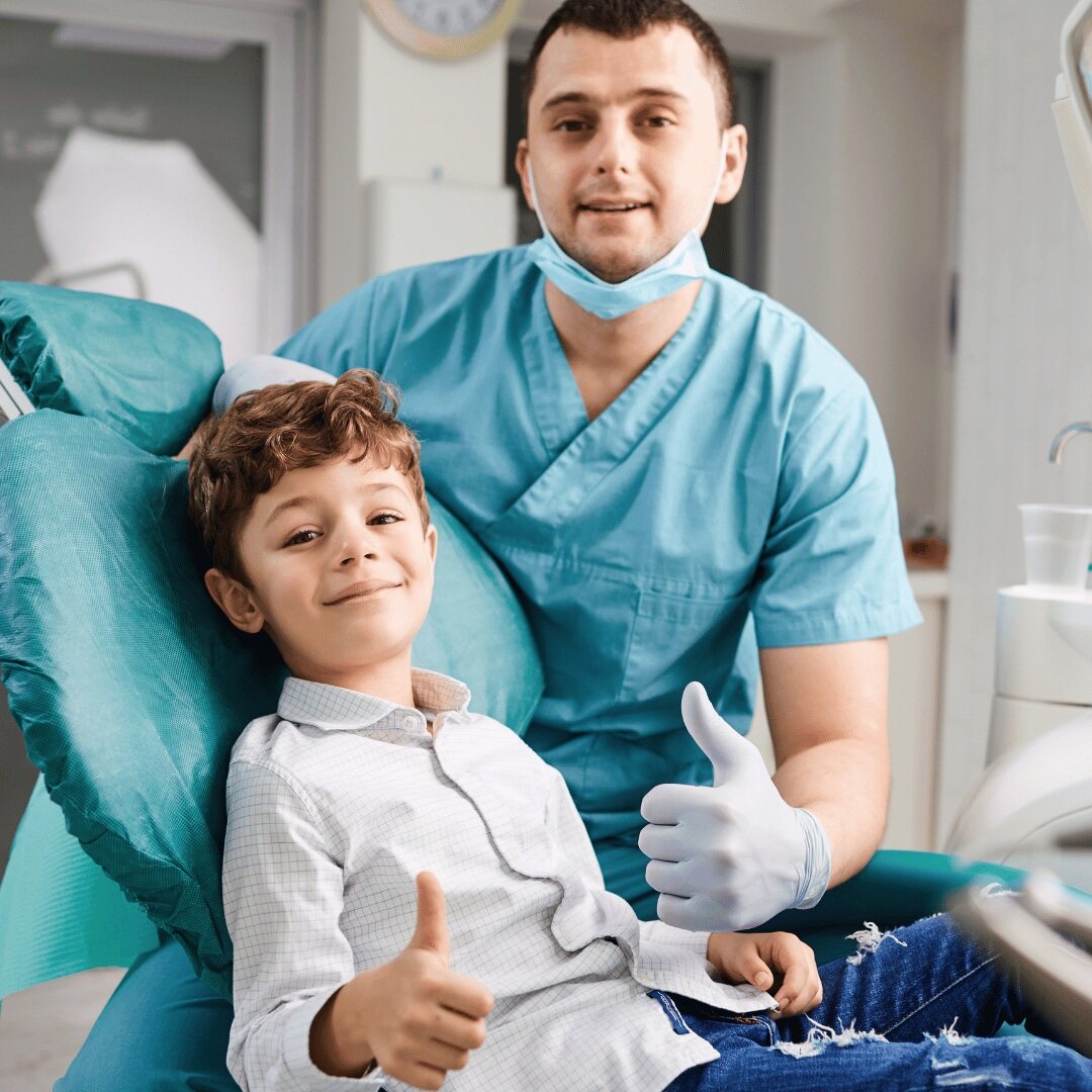 A young patient and his dentist giving a thumbs up after treatment
