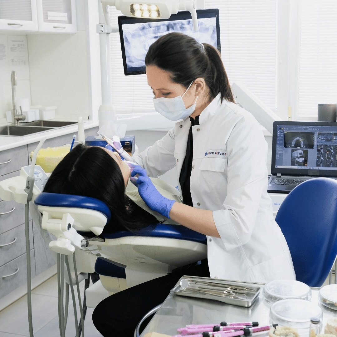 A dentist treating a patient with digital X-rays shown on the monitor behind