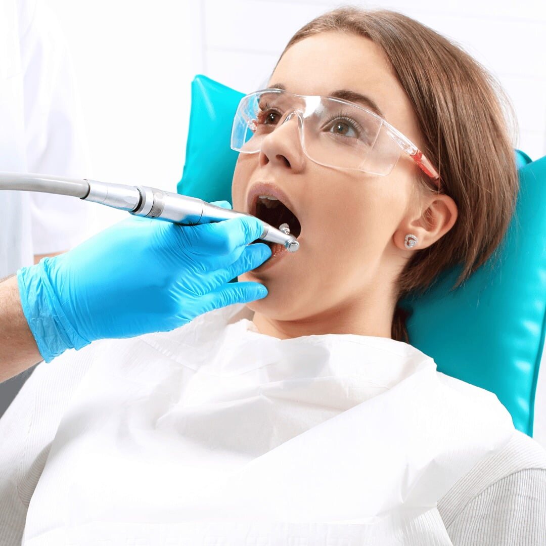 A patient in protective glasses having a tooth treated with a dental handpiece