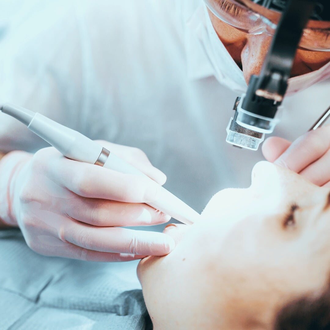 Close-up of a dentist's gloved hands working with a handpiece and mirror