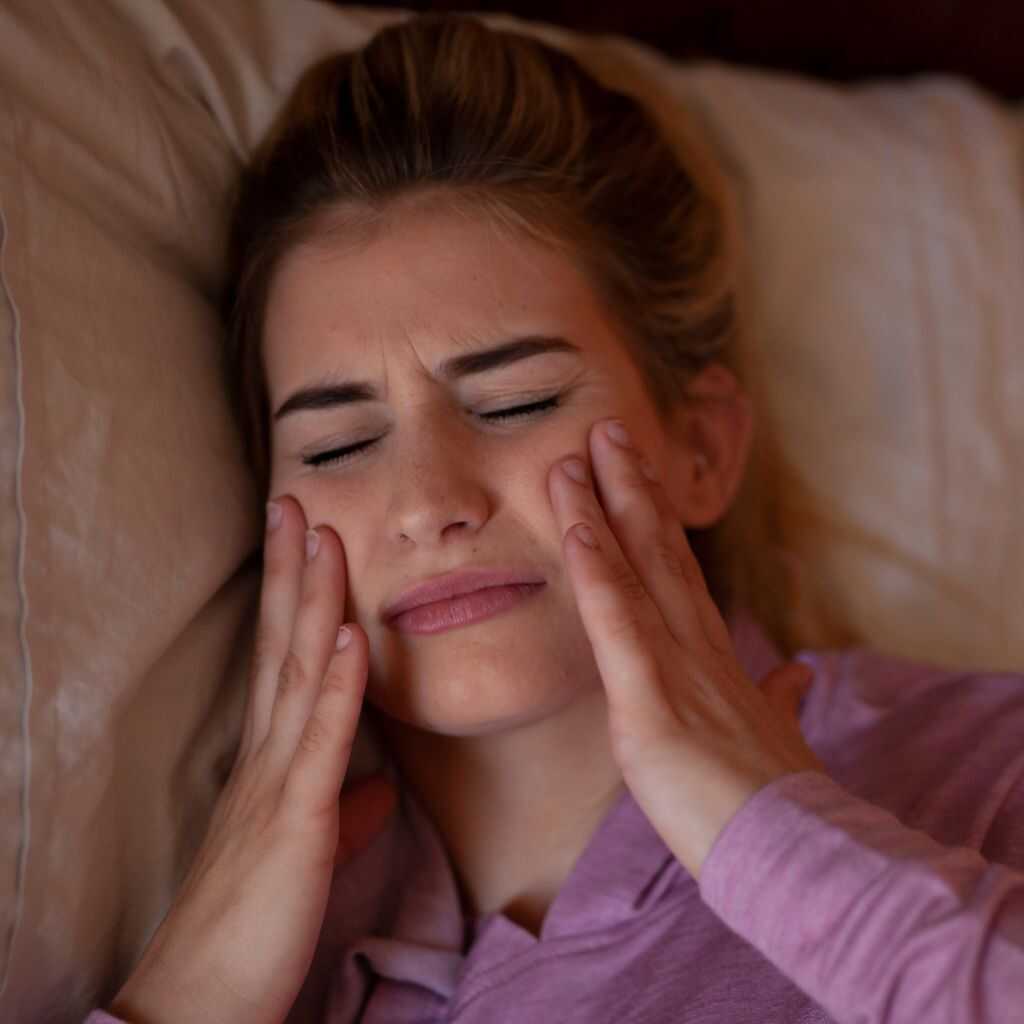 A woman holding both sides of her jaw in pain on waking