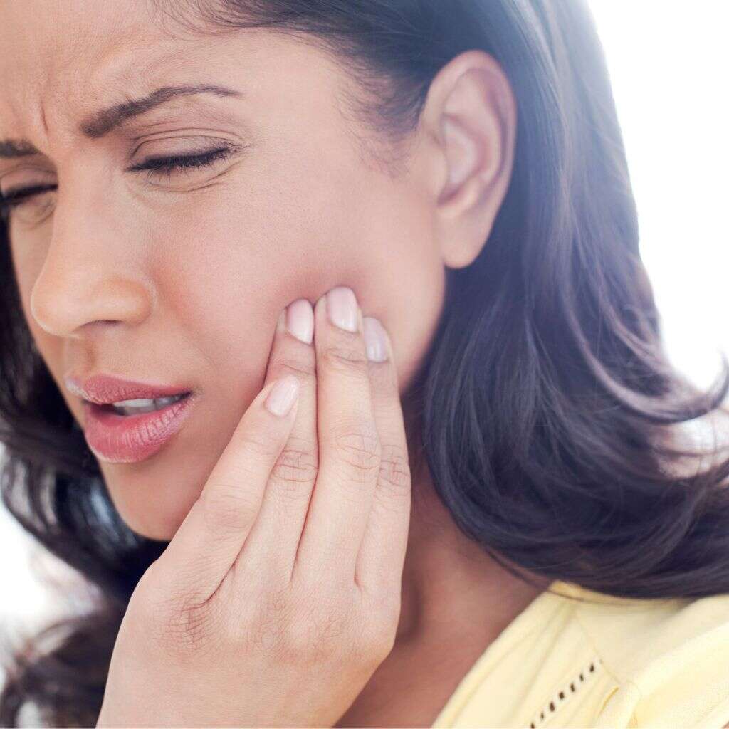 A woman wincing and holding her jaw in pain